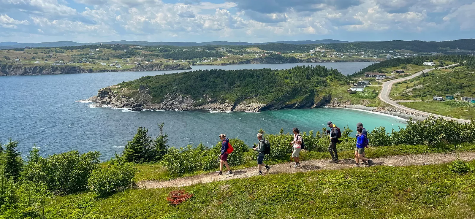 Six guests walking down coastal trail, small beach, ocean, houses in distance.