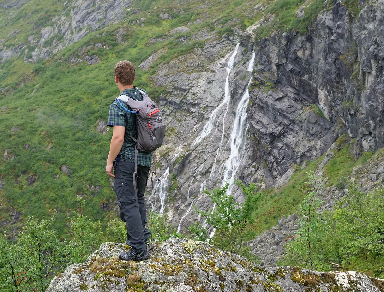 Solo hiker facing away from the camera, looking out at waterfall