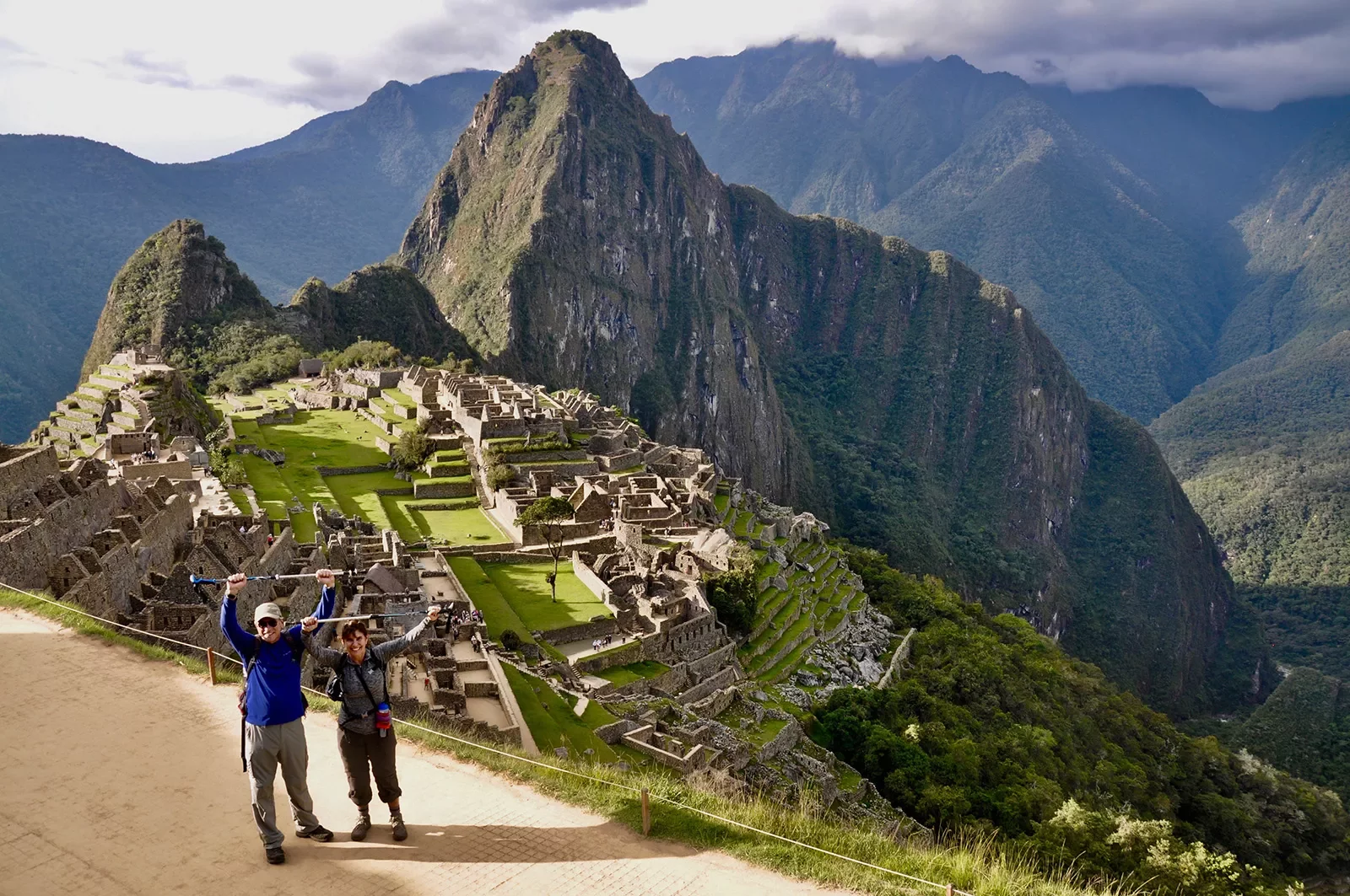 Two guests holding hiking poles over their heads in celebration, Machu Picchu in background.