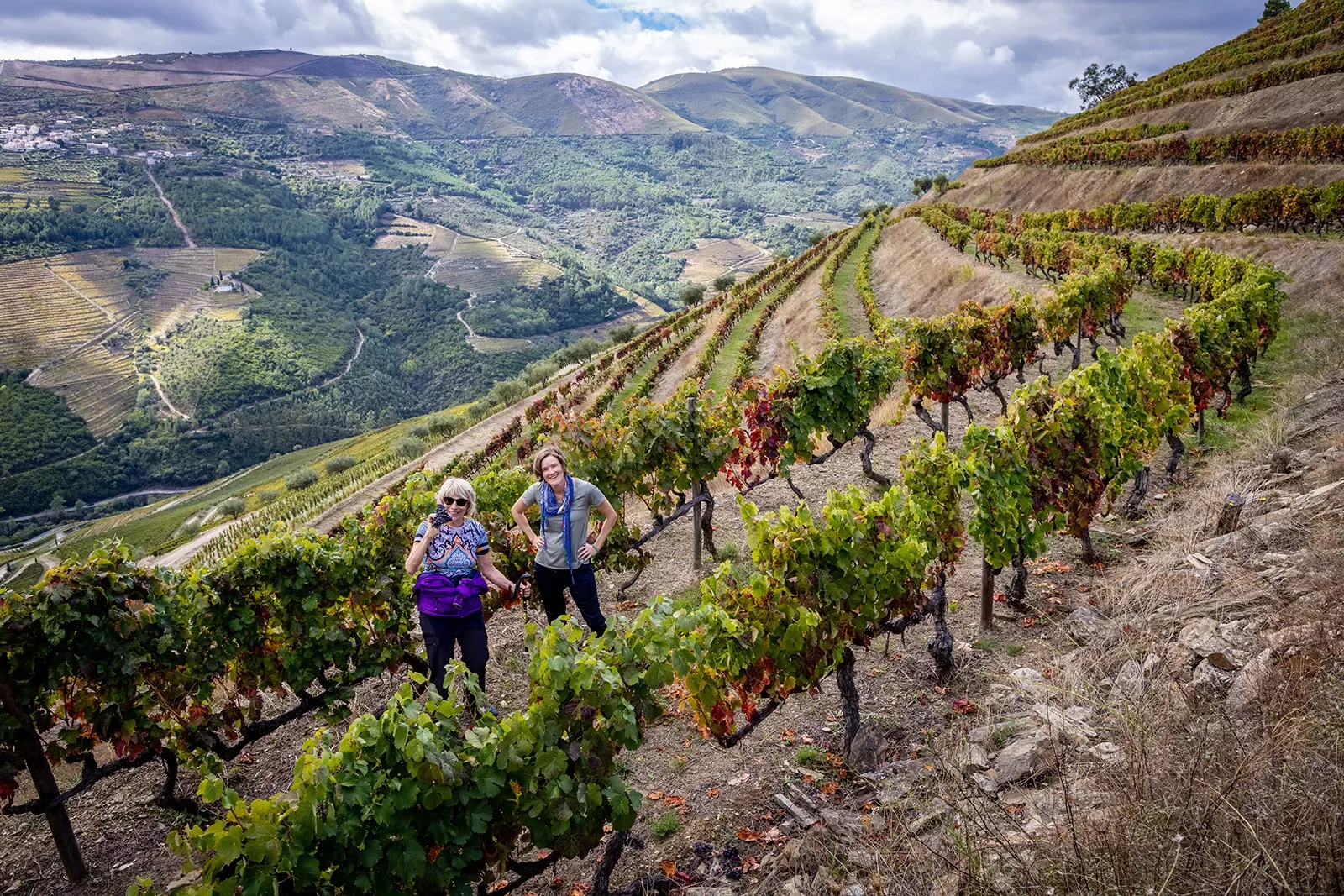 Two women posing in a vineyard on the side of a mountain