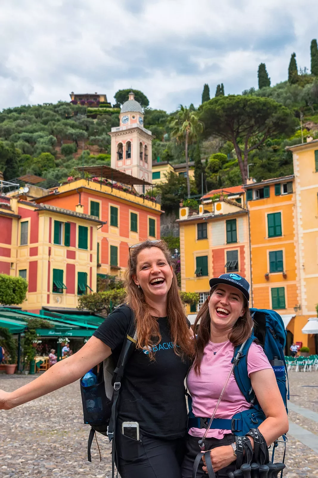 Two smiling guests in front of colorful buildings.