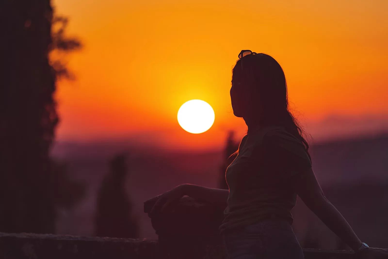 Woman backlit in front of vibrant sunset horizon.