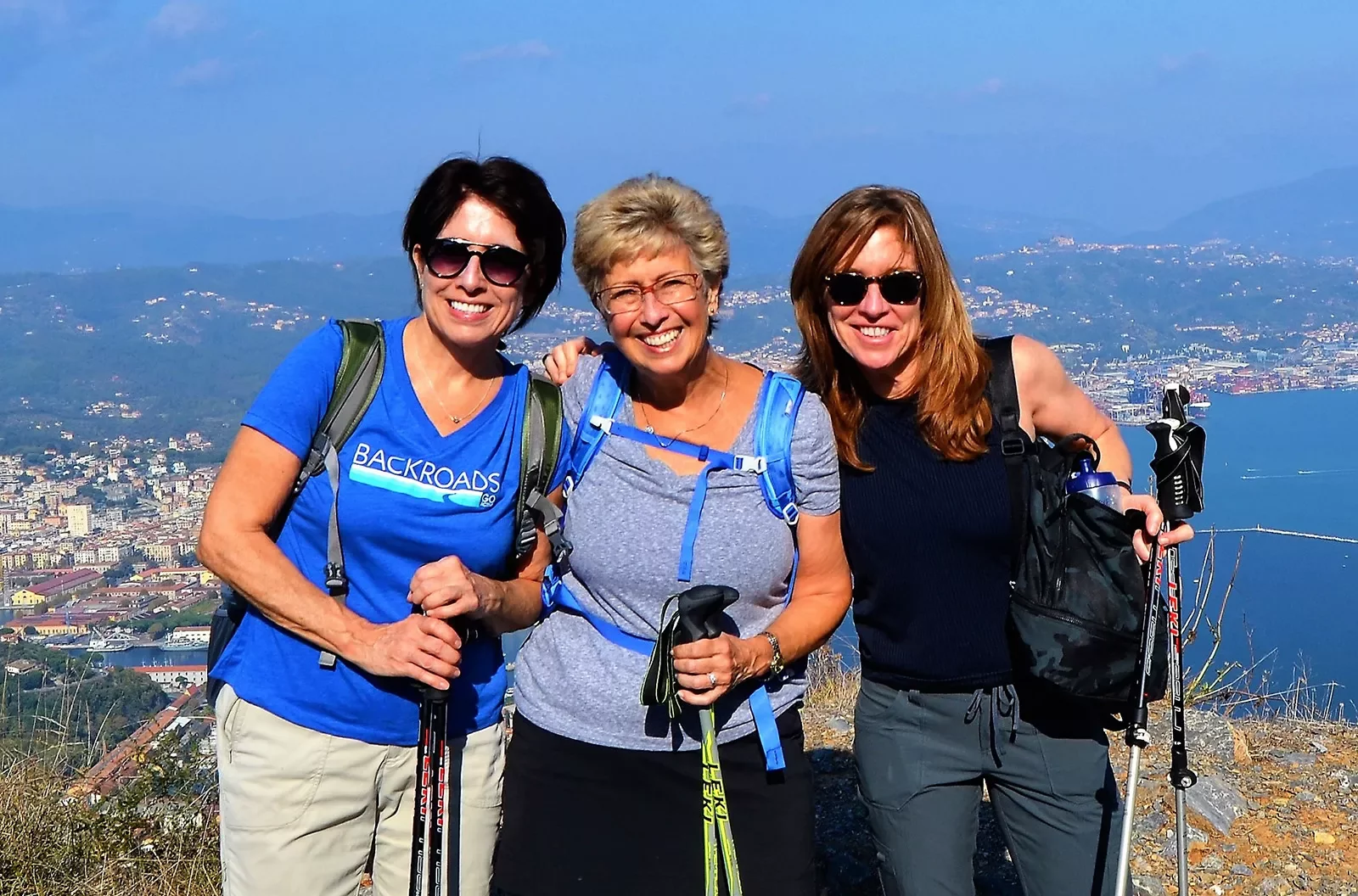 Three women posing together with Italian landscape behind them.