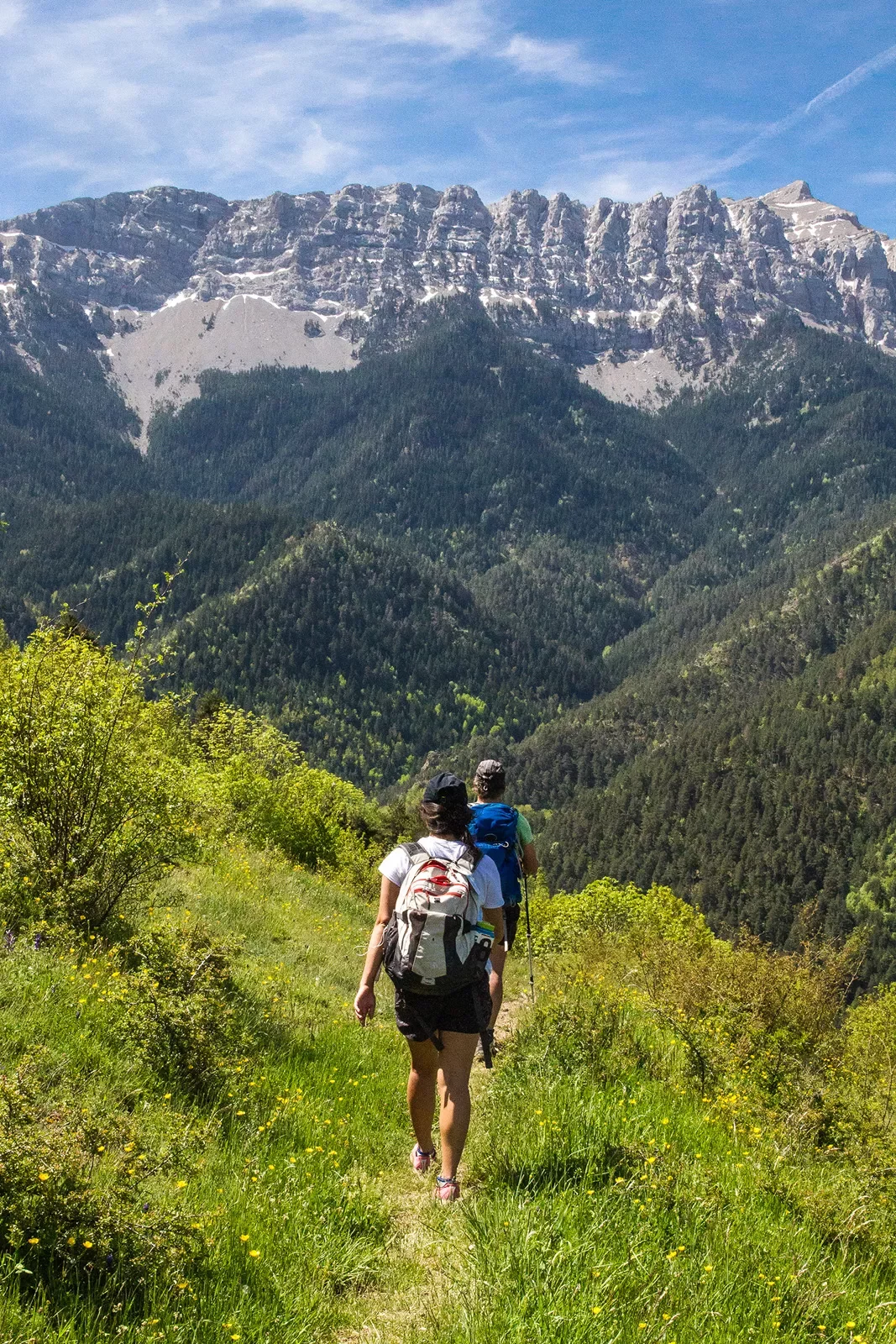 Two guests on mountain trail, walking towards large range.