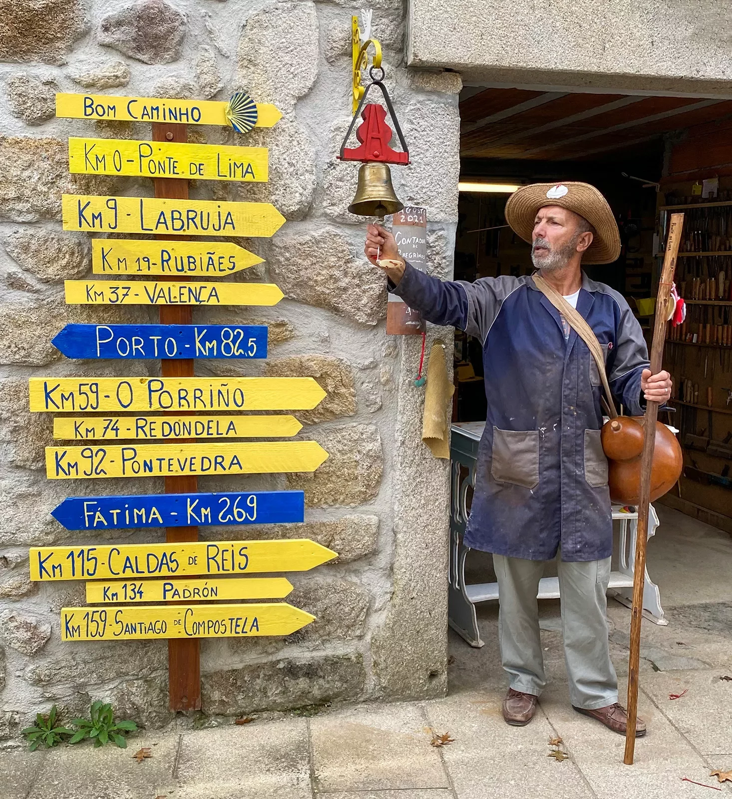 Local in hiking gear ringing bell, assortment of direction signs to his right.