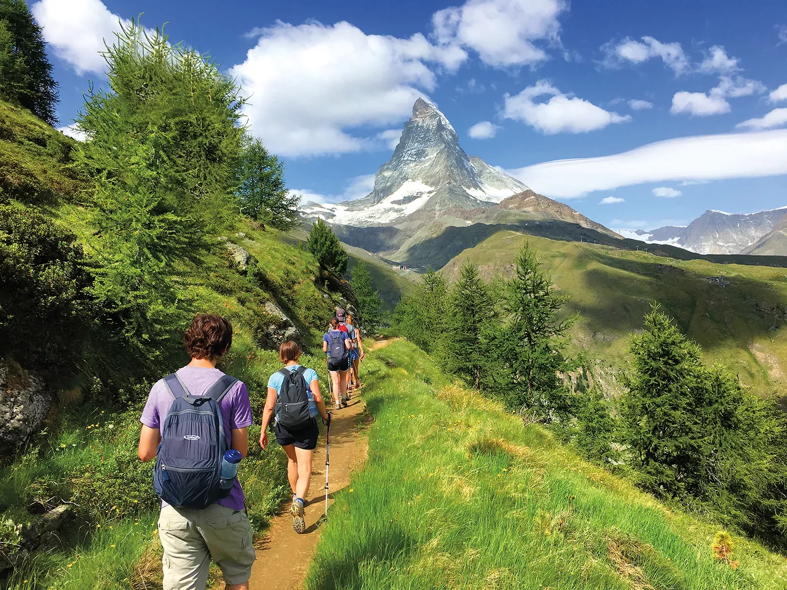 Group of guests on hillside trail, Matterhorn in distance.