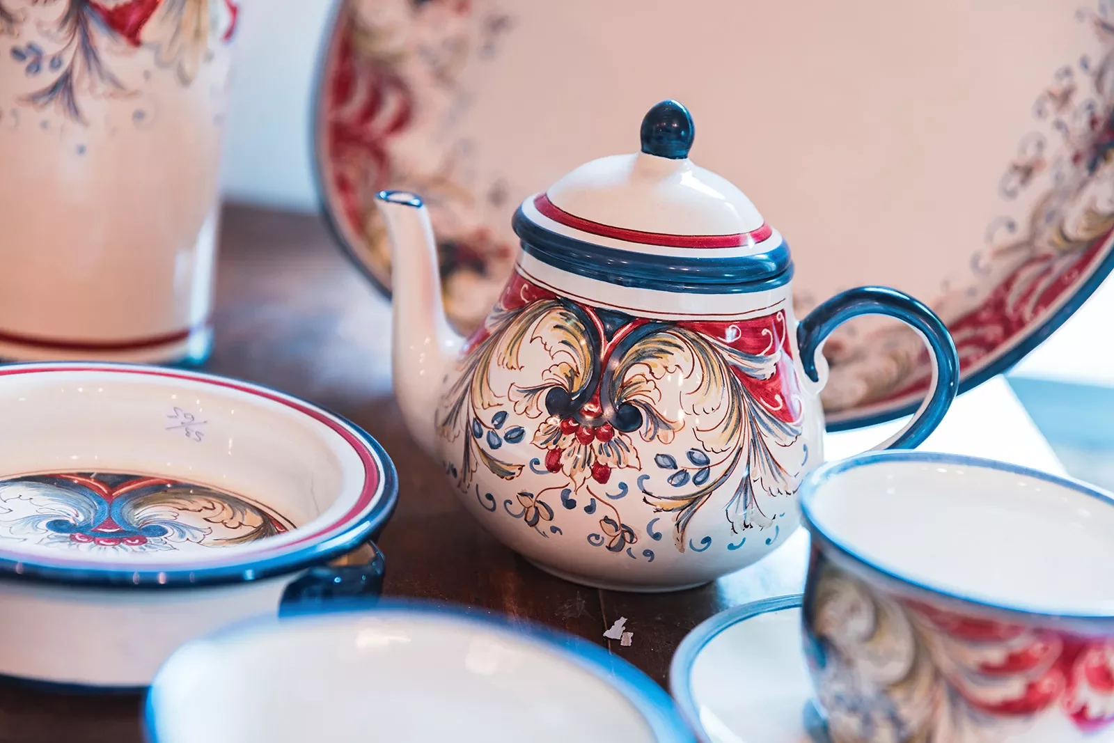 red, white and blue teapot with cups surrounding