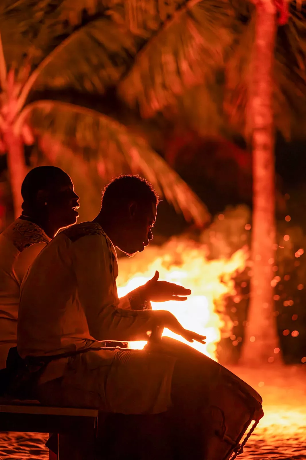 Two men playing bongos around a campfire