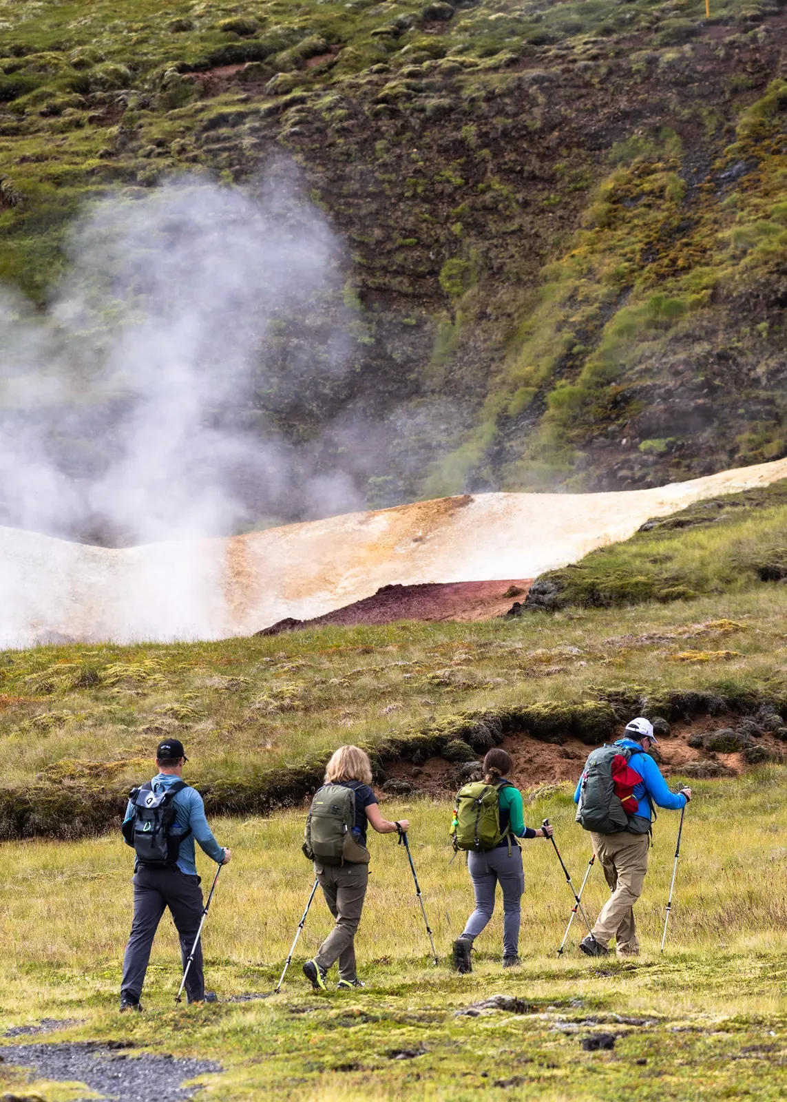 Four hikers with hiking sticks walking past a steaming geyser