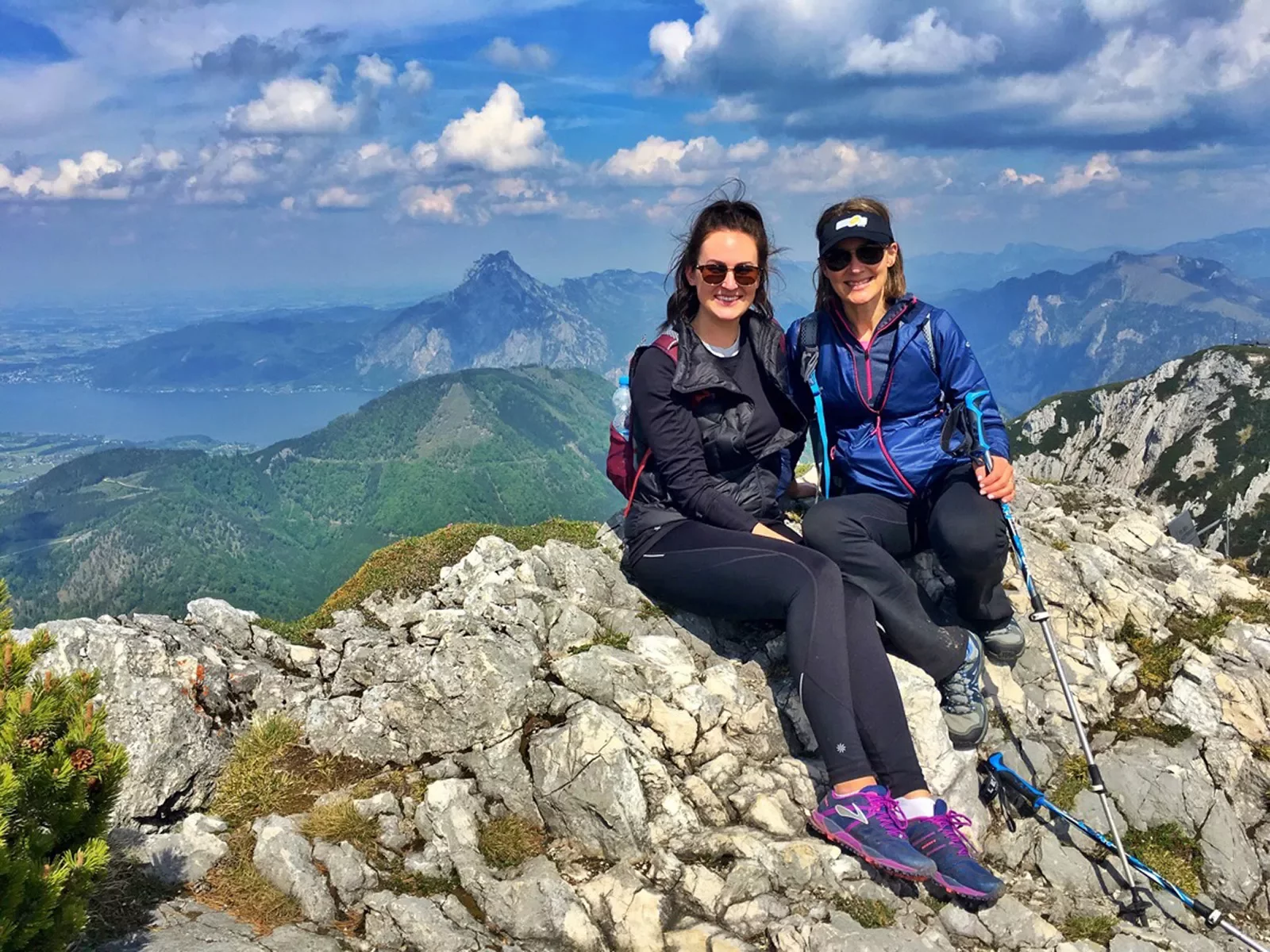 Two women sitting on a pile of rocks at the top of a mountain
