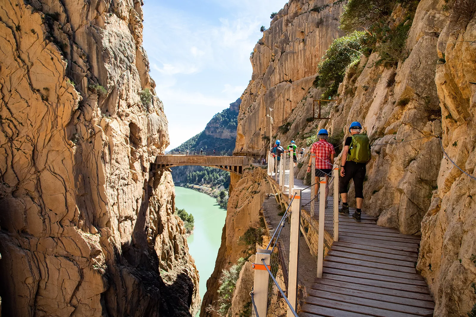 Group of people walking on a wooden bridge in between two large cliffs