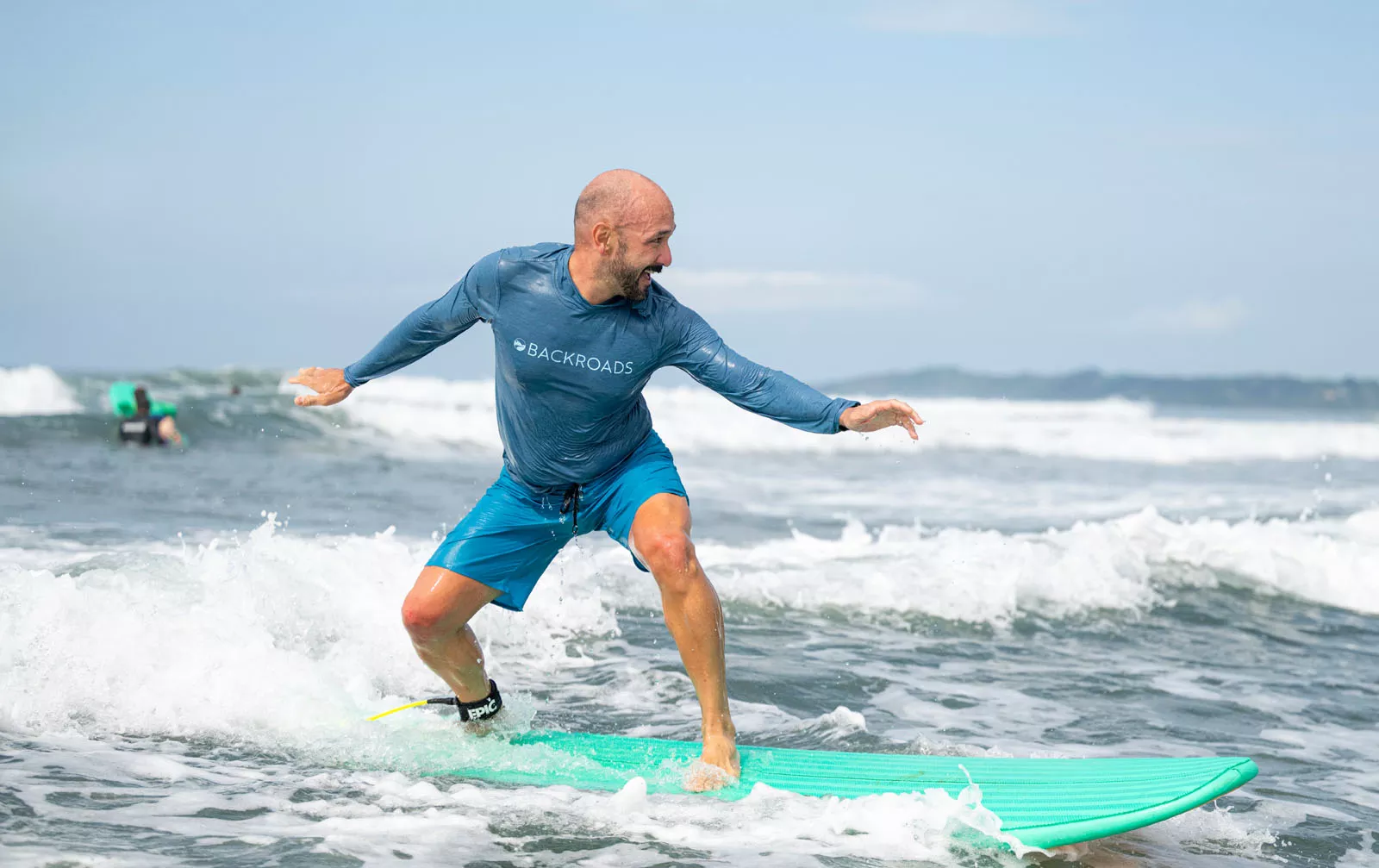 Man smiling while standing on top of a surfboard