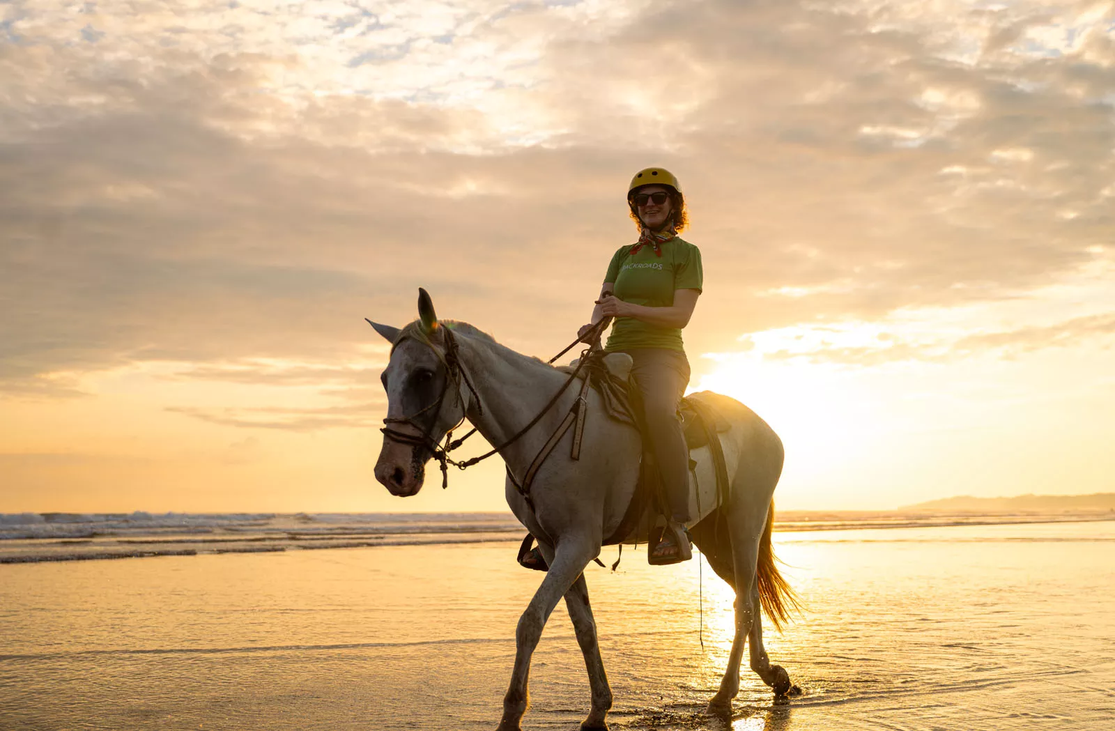 Woman smiling while riding a white horse on a beach