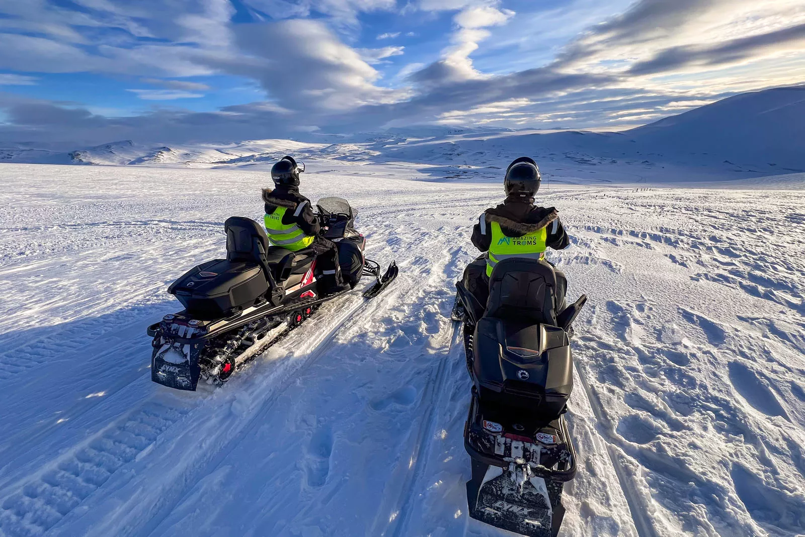 Two people riding on snow mobiles in a vast valley of snow