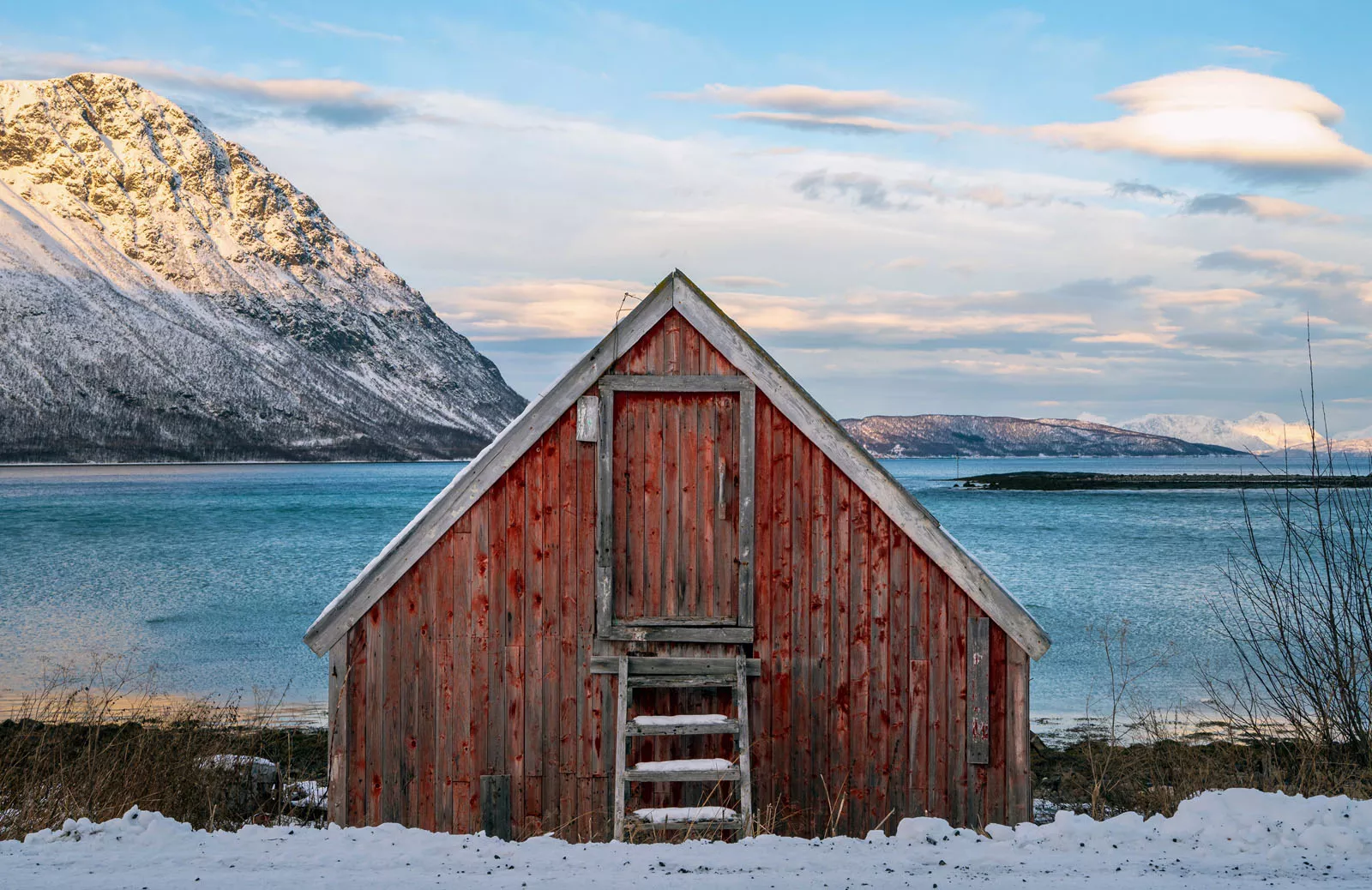 Red shed in a valley of snow with the ocean in the background
