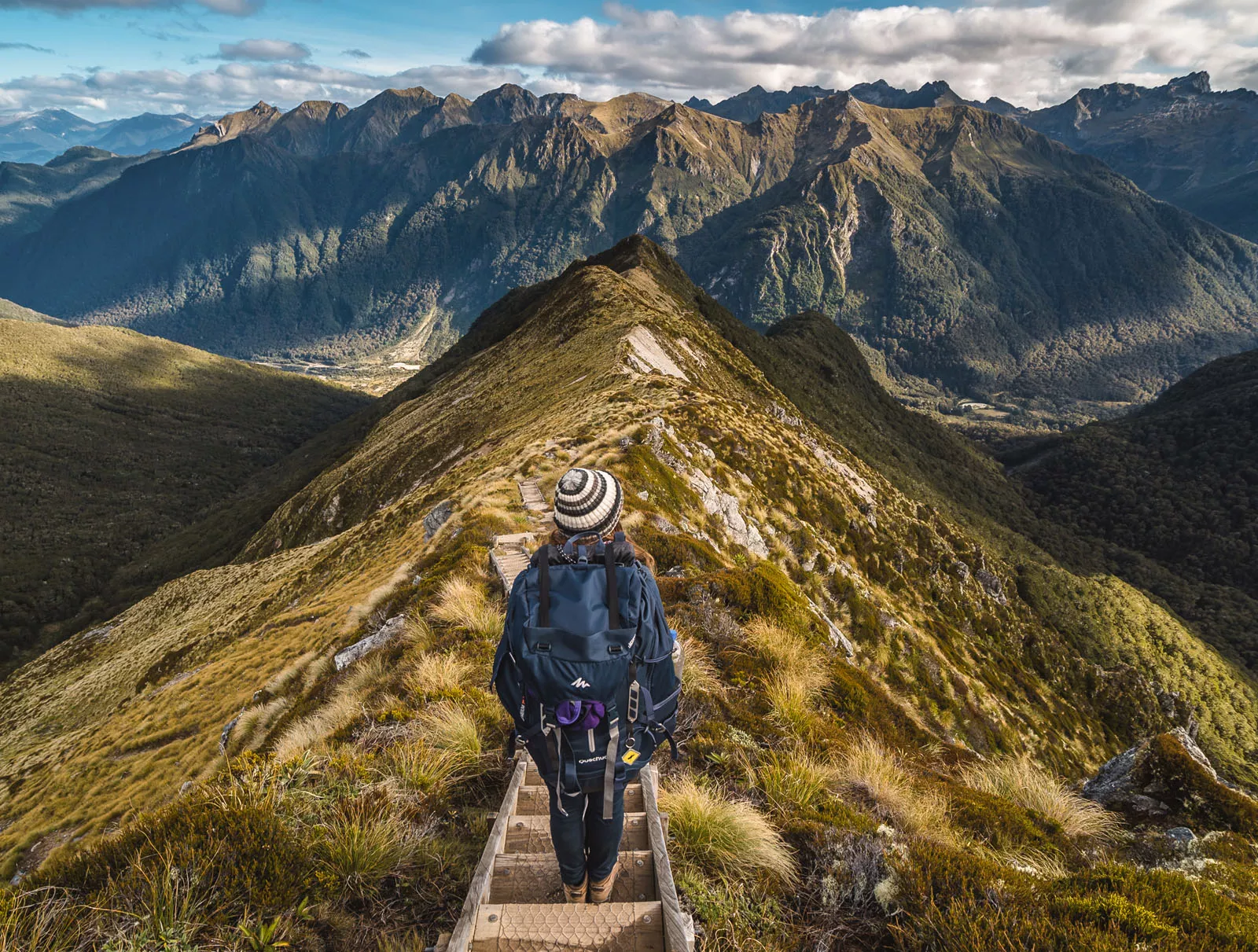 Woman descending a mountain with large mountains in the background