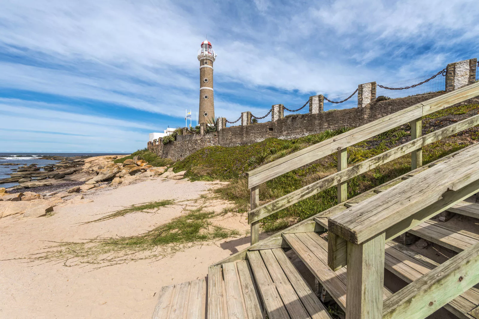 Beach with a wooden staircase and a lighthouse in the background