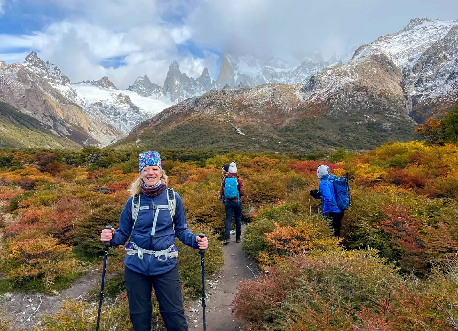 Woman smiling while holding hiking poles, with large mountains in the background