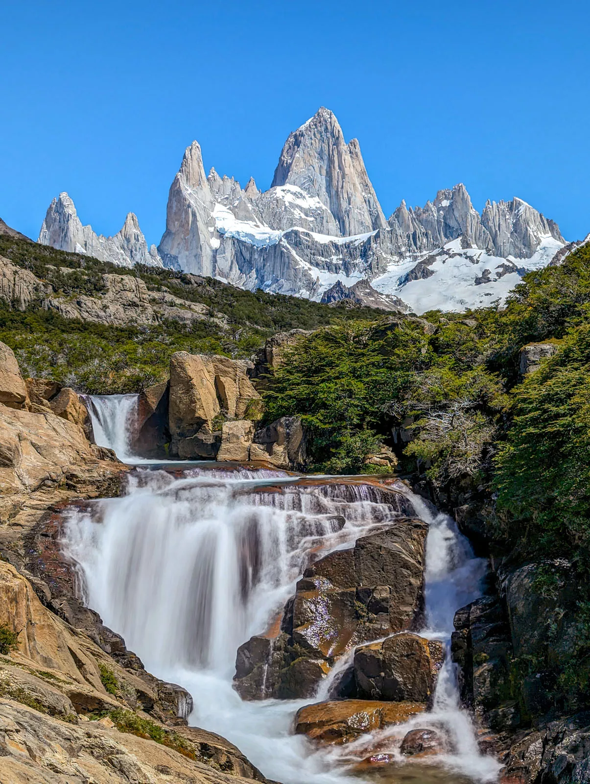 Active waterfall on large boulders with tall mountains in the background