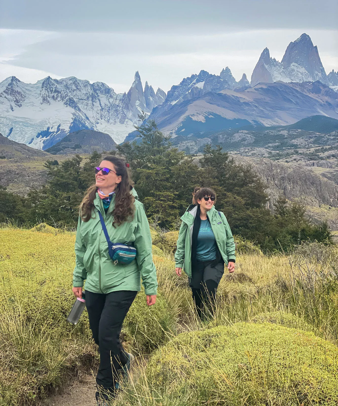 Two women smiling while walking in a field with tall weeds