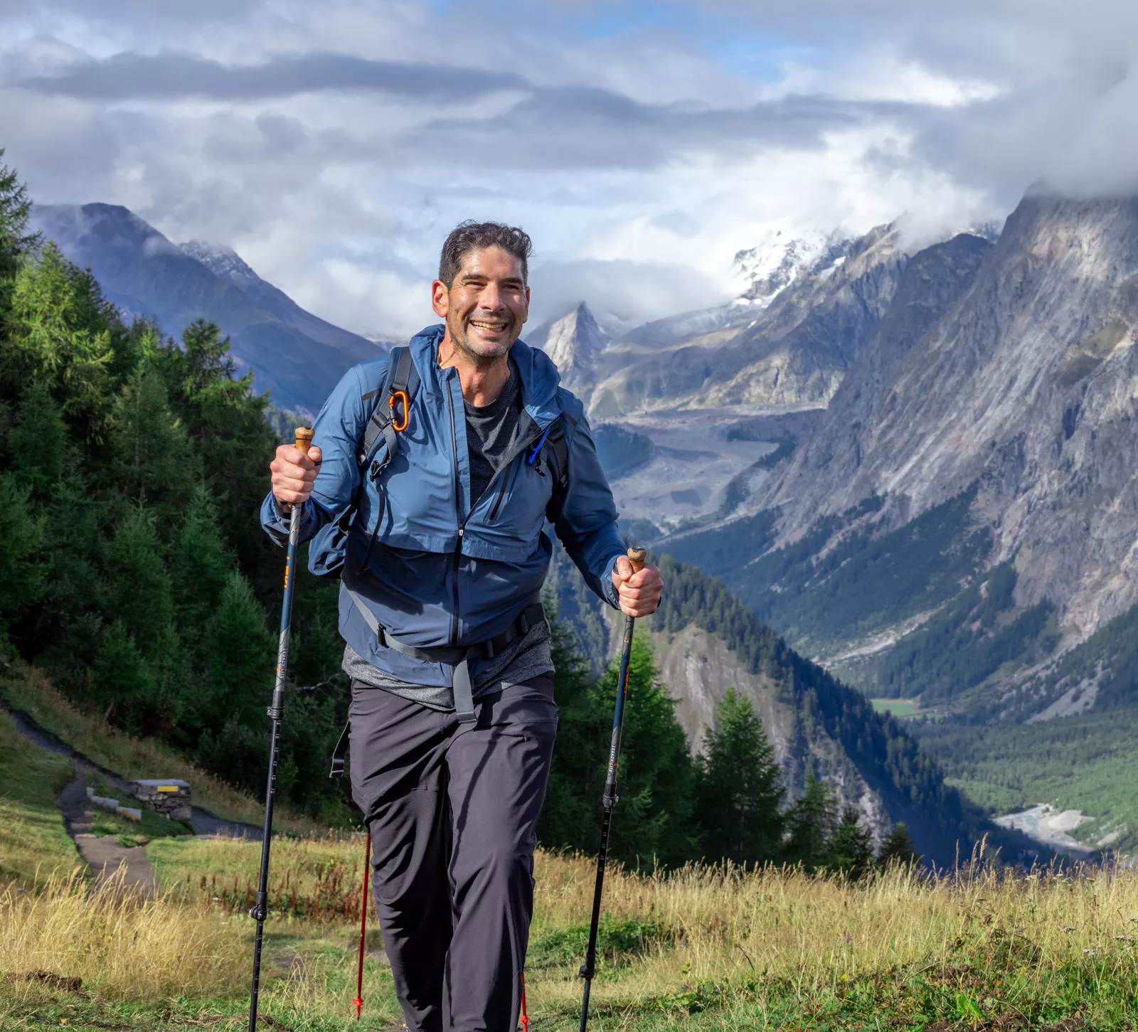 Man with hiking poles, walking on a grassy valley while smiling
