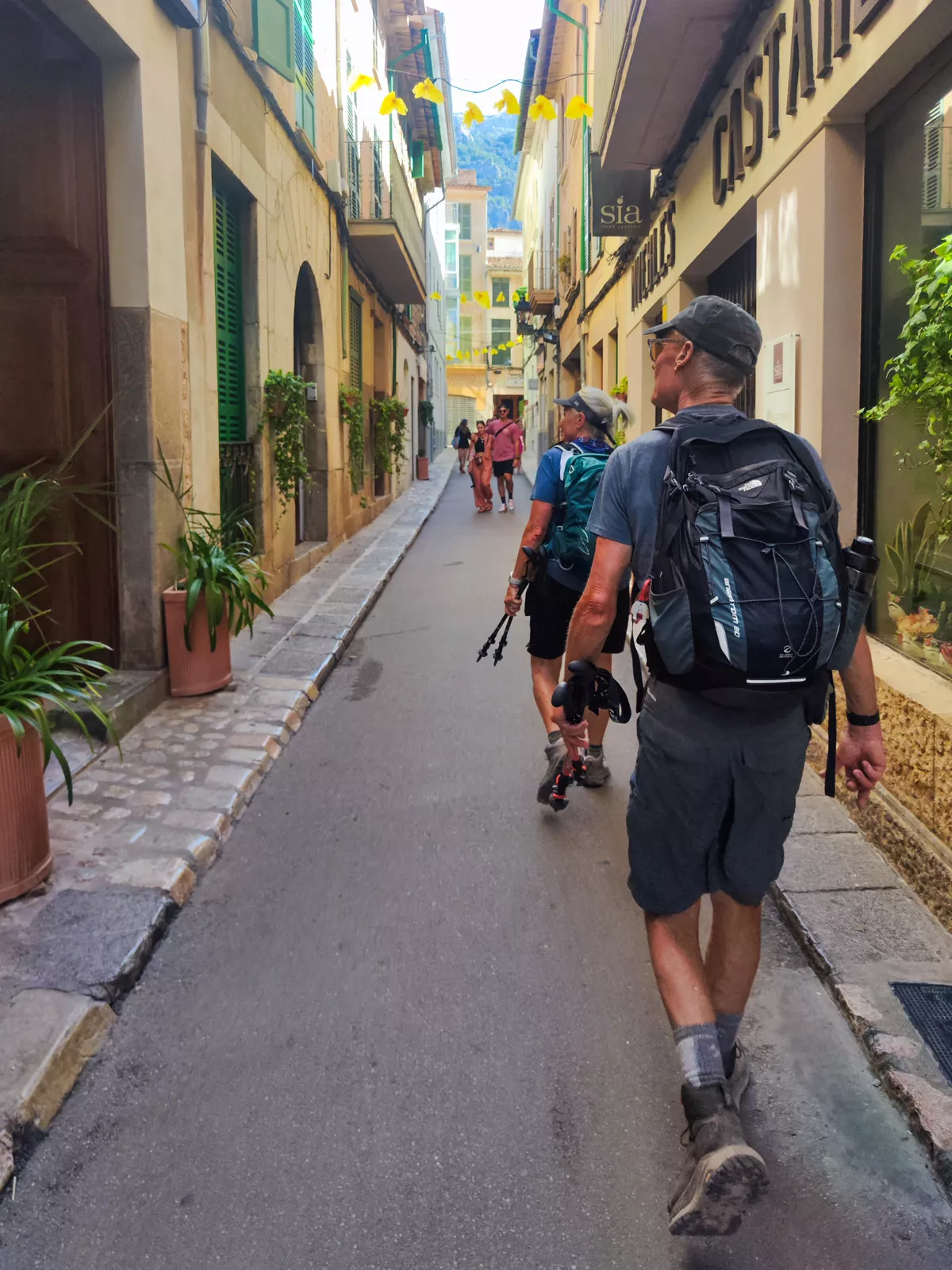 Group of men wearing backpacks, walking through a town alleyway with large buildings on either side