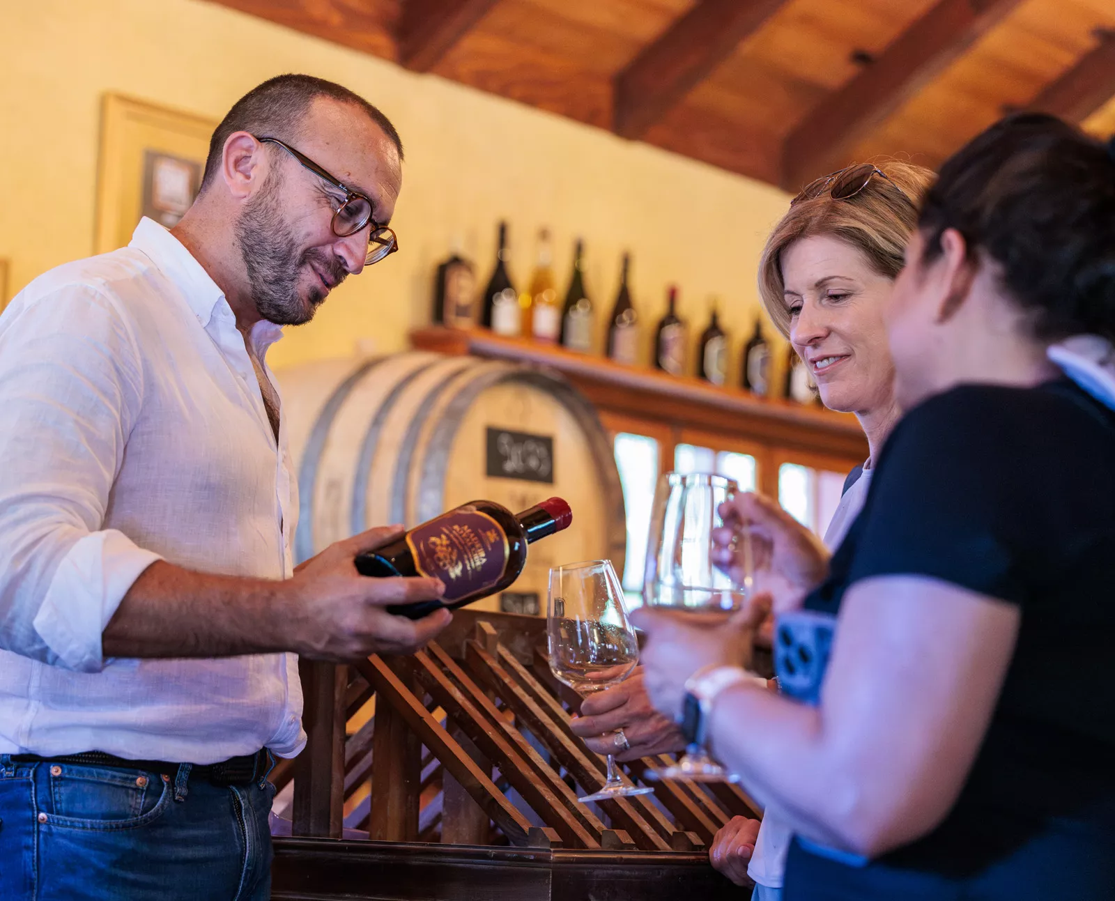 Man pouring wine into the glasses of two women