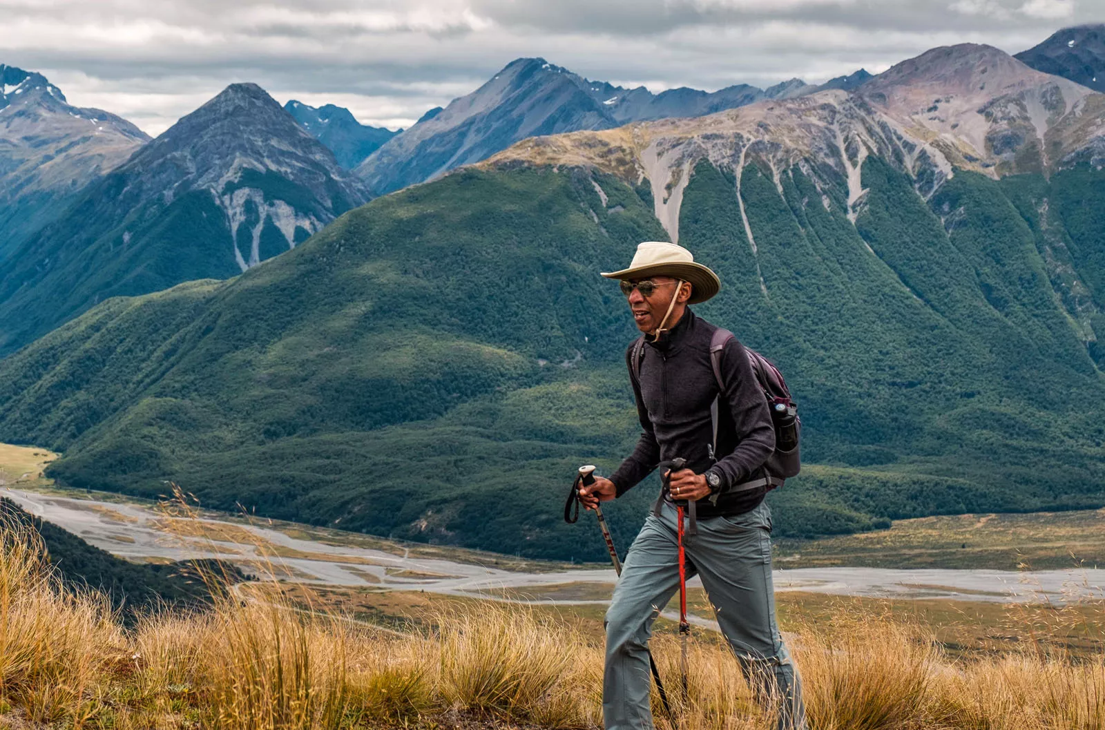 Man with hiking poles, walking on a trail with a lake in a distance