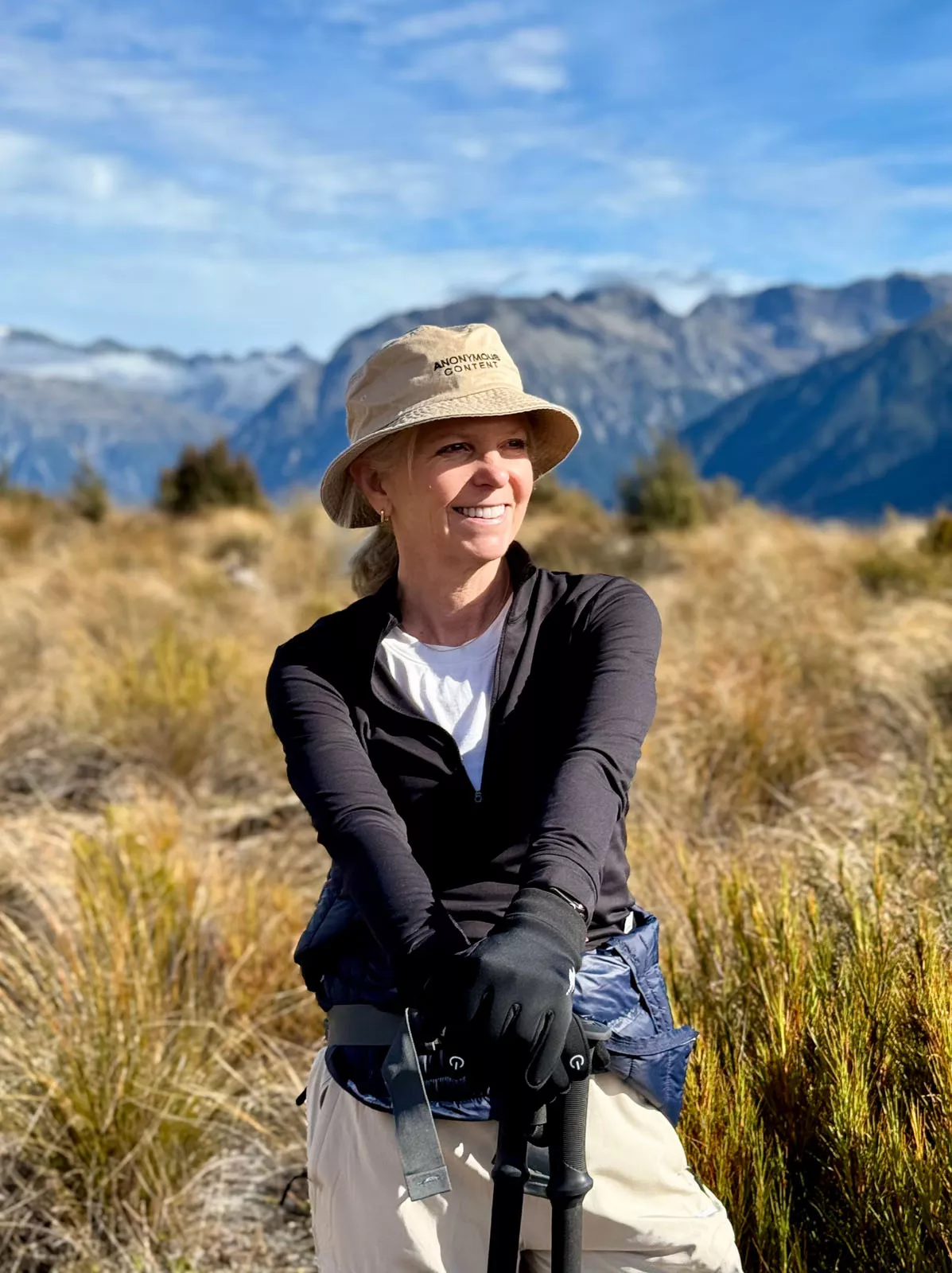Woman smiling in a field with large mountains ion the distance