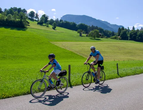 Father and son biking on an empty road, with large grass fields behind them