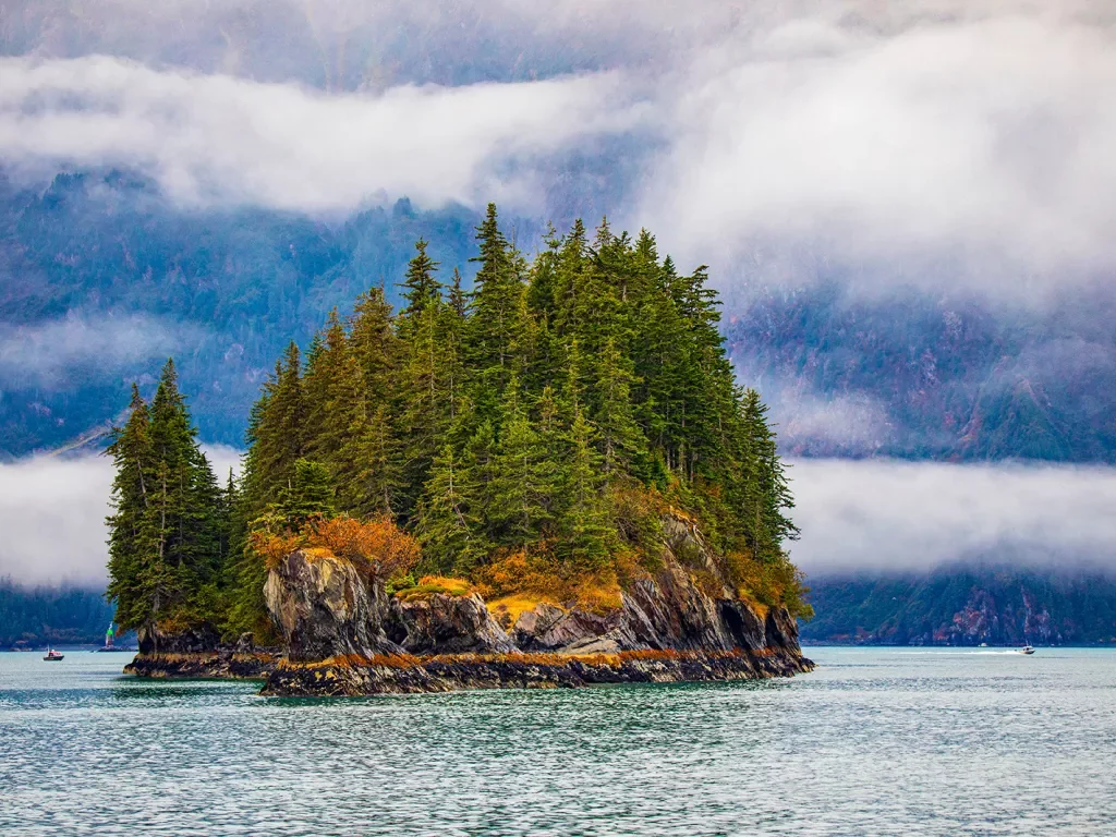Wide shot of small rocky, tree covered island among foggy lake.