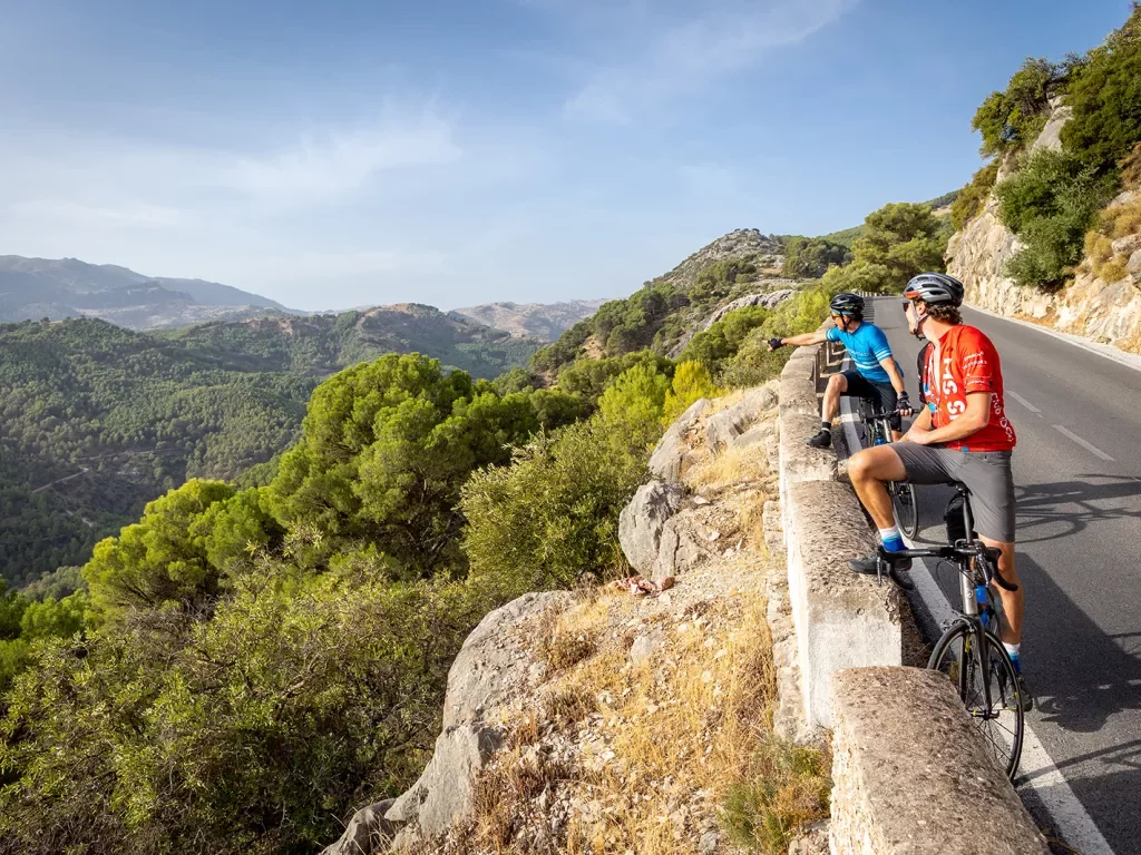 Bikers resting with bikes on side of a road in Spain, admiring a view.