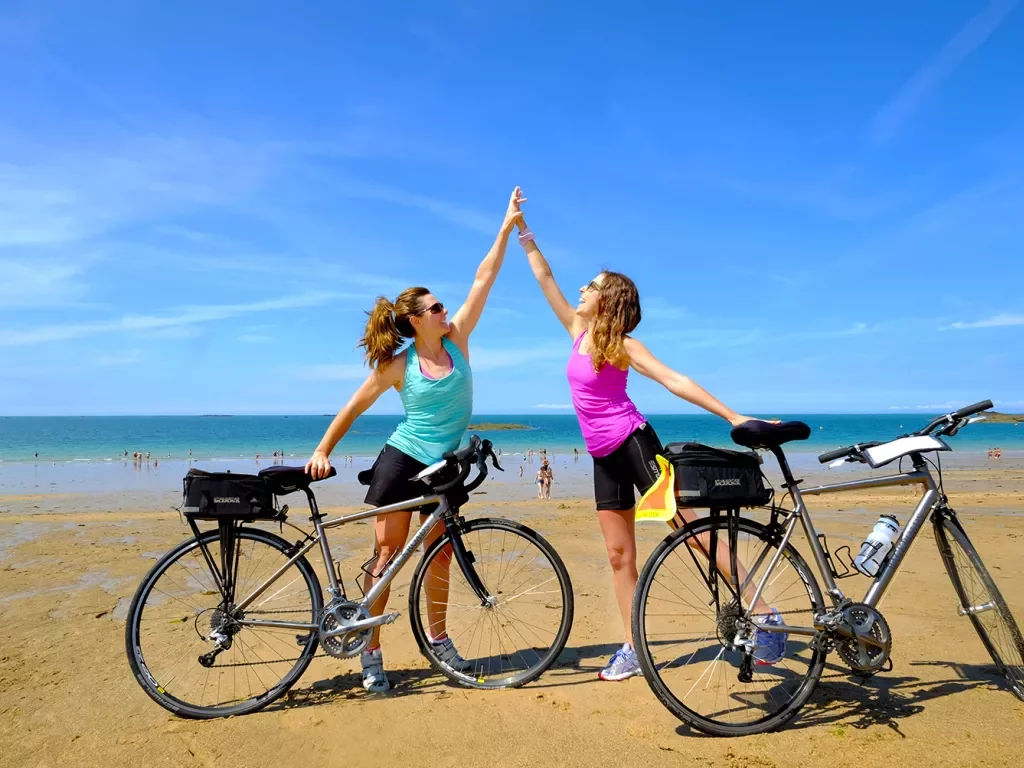 Two Backroads Guests High Fiving on Beach with Bicycles 