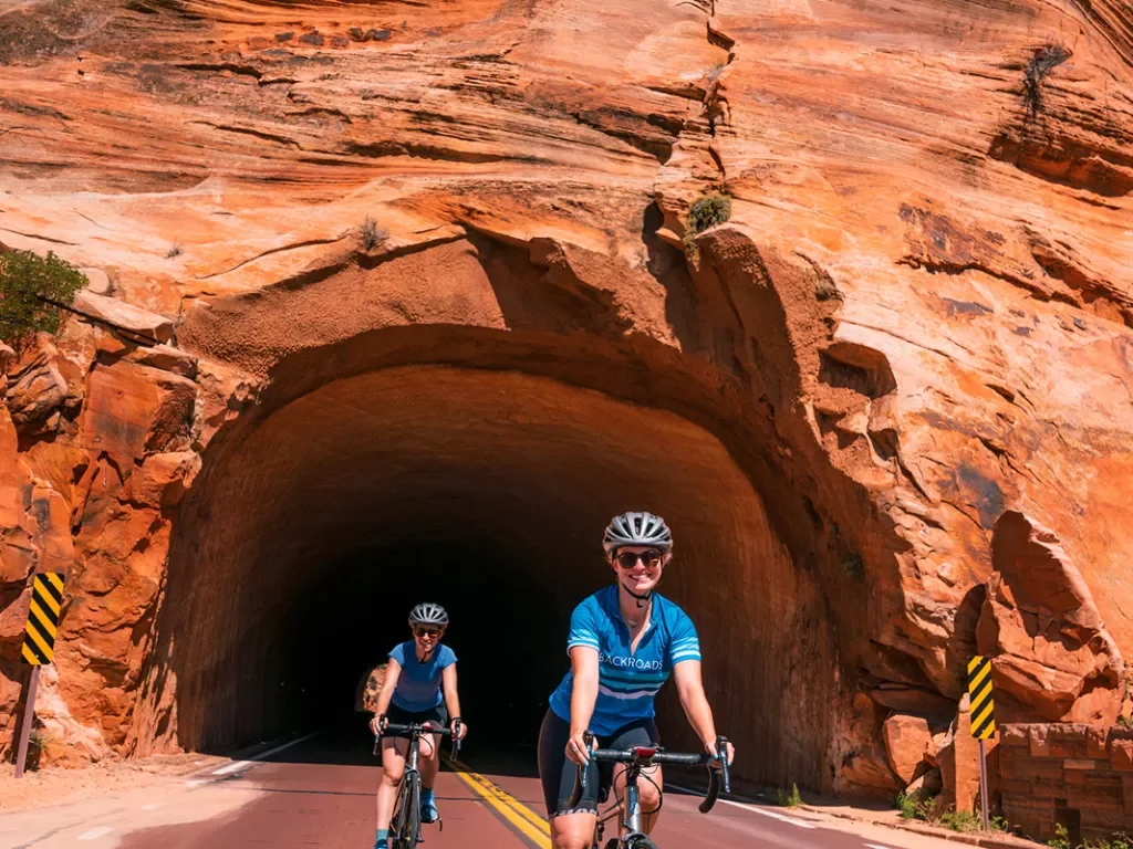Two bikers emerging out of rock tunnel