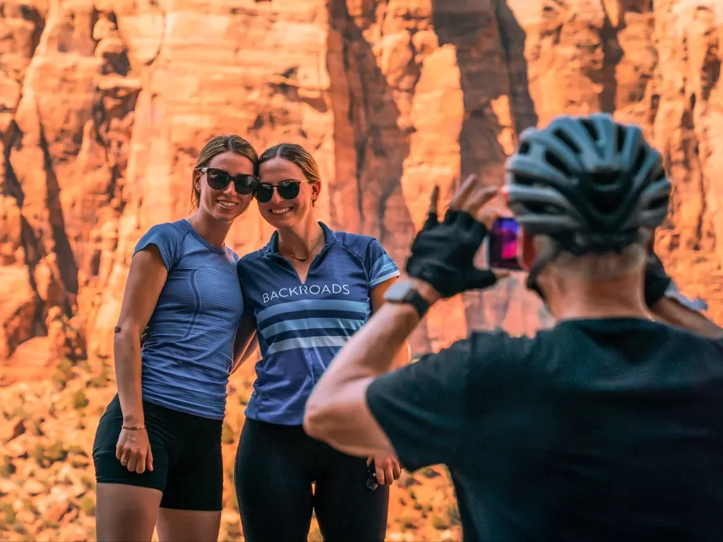 Guest taking photo of two others, all in bike gear, orange cliffs behind them.