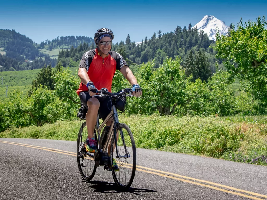 Guest cycling up grassy road, mount hood for off in background.