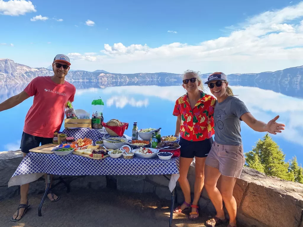 Three guests next to lunch table, large lake in background.