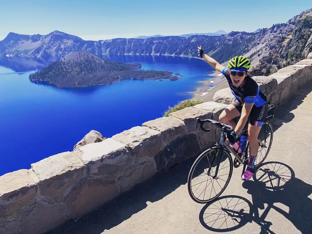 Guest cycling and gesturing towards Crater Lake on her right.