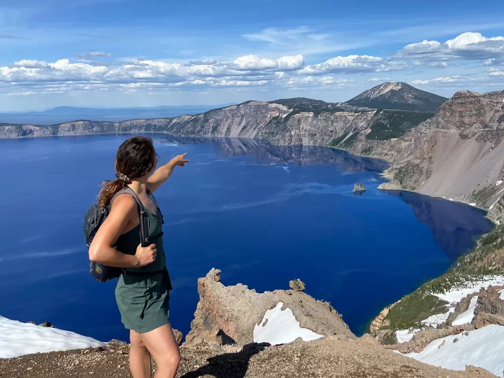 Guest on cliff's edge, pointing towards Crater Lake.