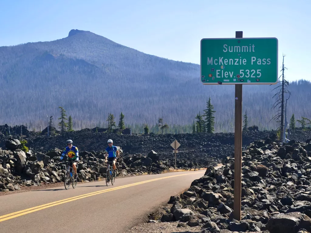 Two guests cycling past "MCKENZIE PASS" sign.