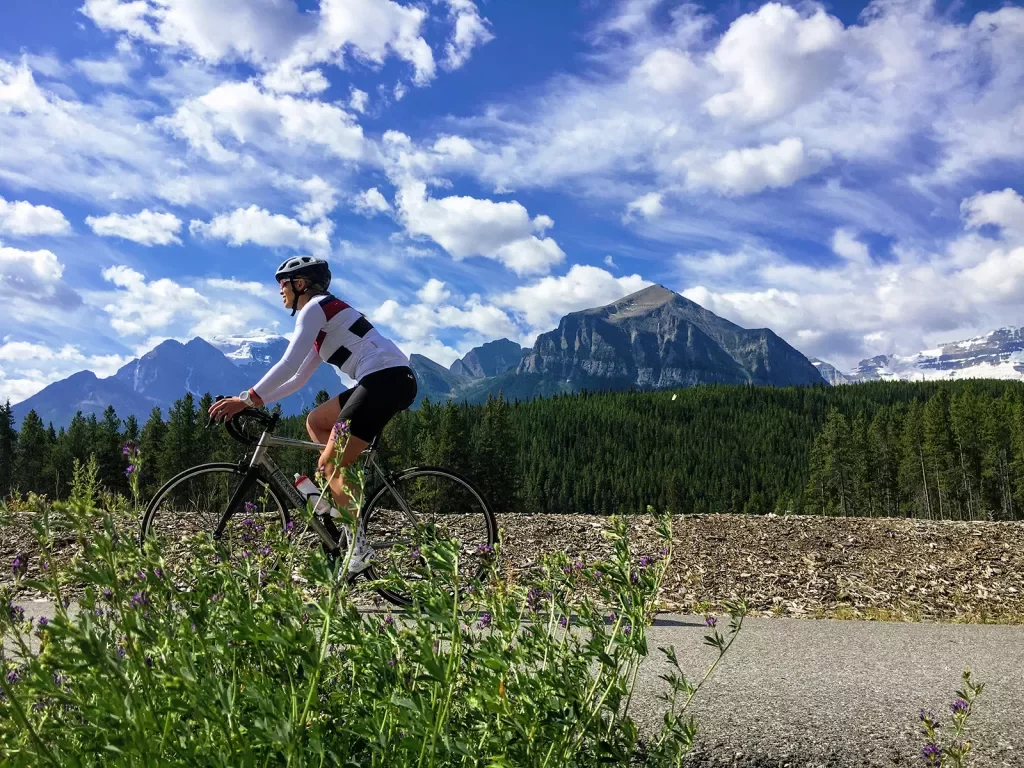 Guest cycling on meadow road, mountain and clouds in background.