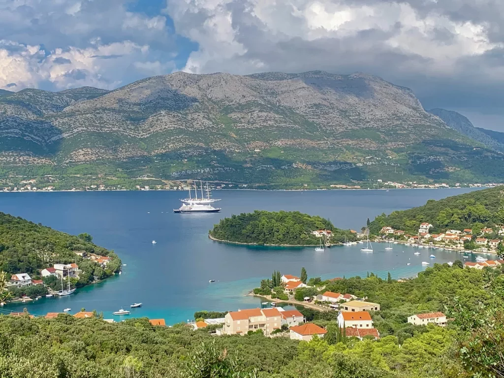 Wide shot of coastal Croatian town, mountains, large river, boat behind.