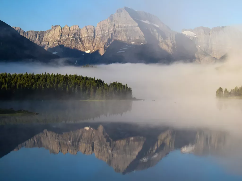 Fog wrapped around mountain in the background of reflective lake