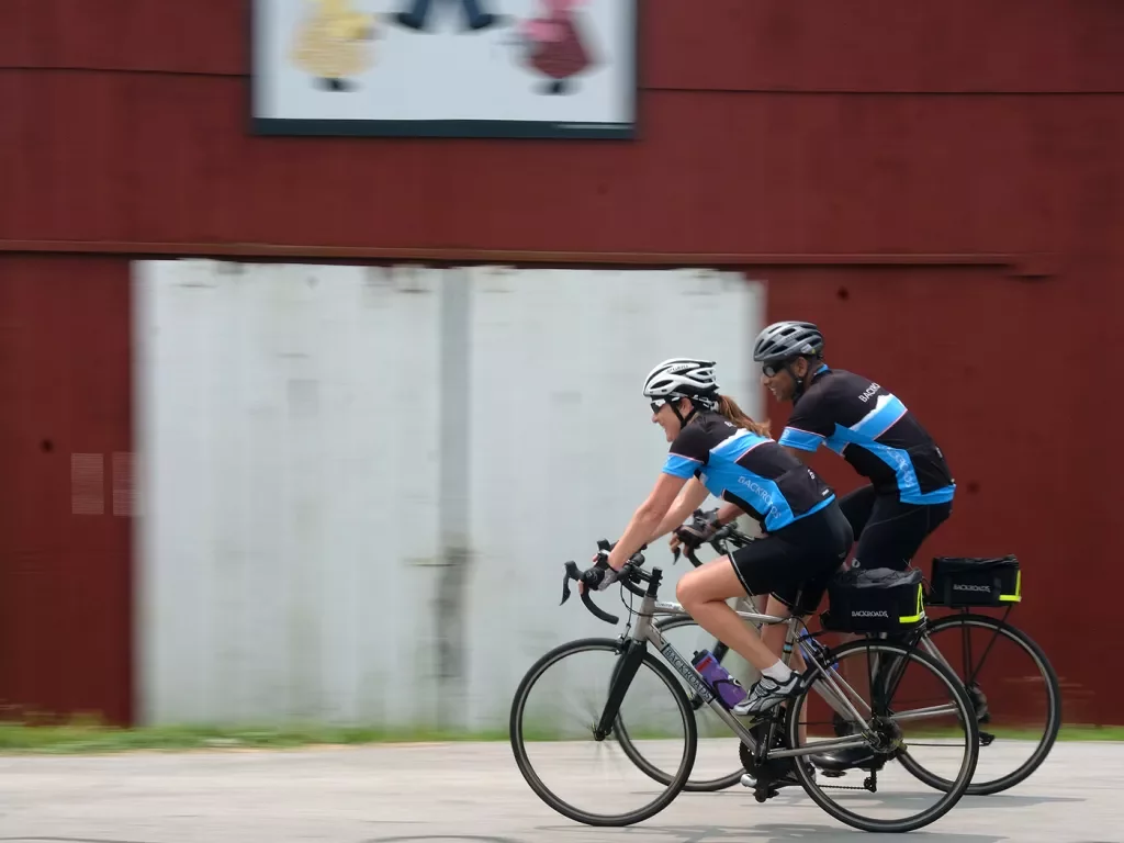Two guests cycling past red barn.