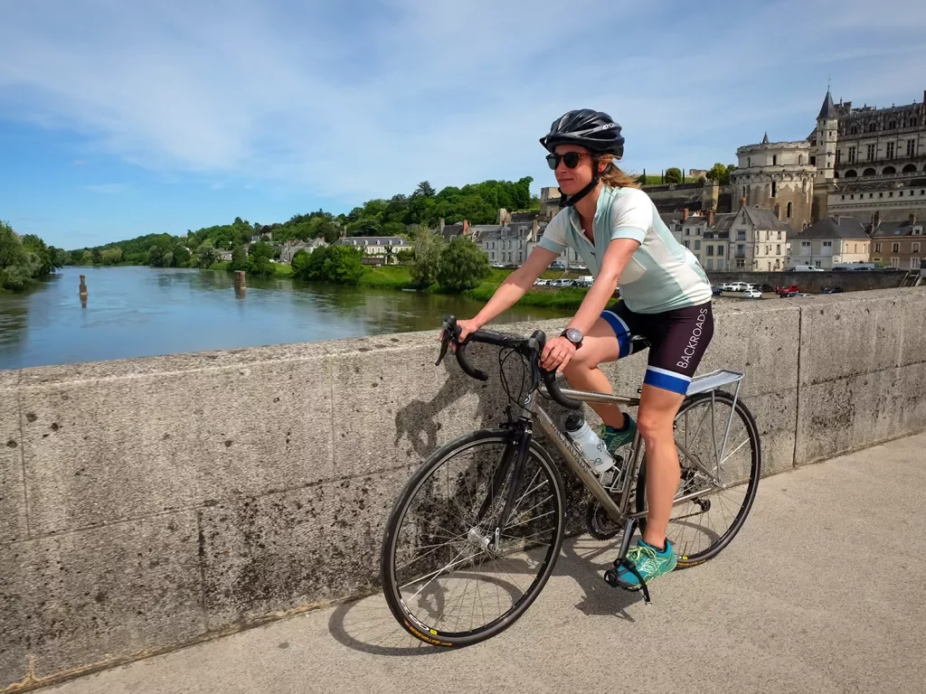Guest cycling over concrete bridge, river, riverside town behind her.