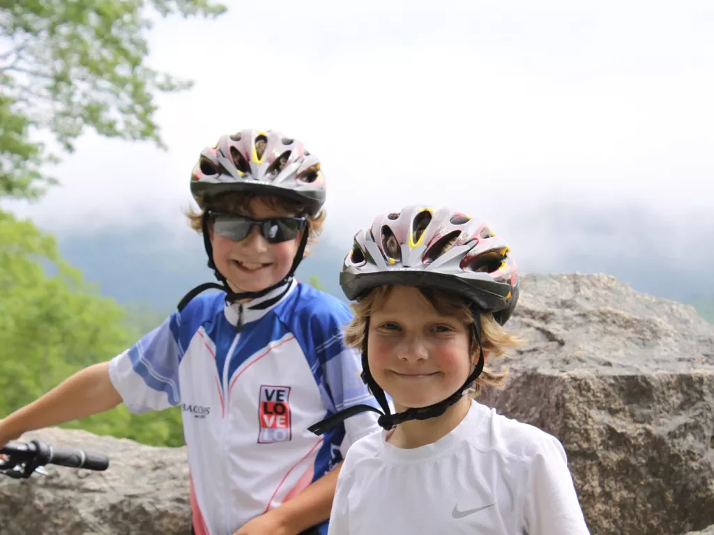Two child guests in helmets smiling for camera, foggy vista behind them.