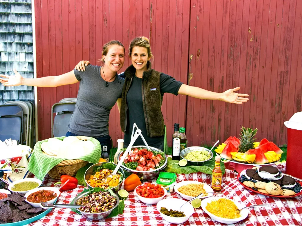 Two people posing behind lunch spread.
