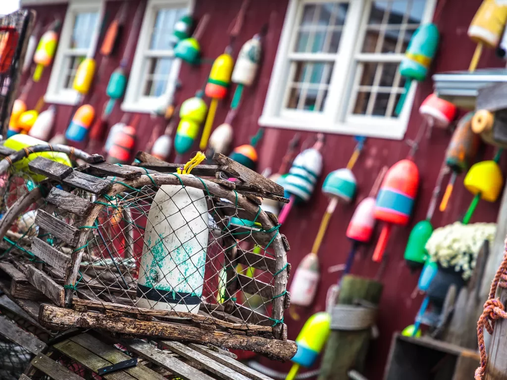 Shot of lobster trap in front of red fishing shack.