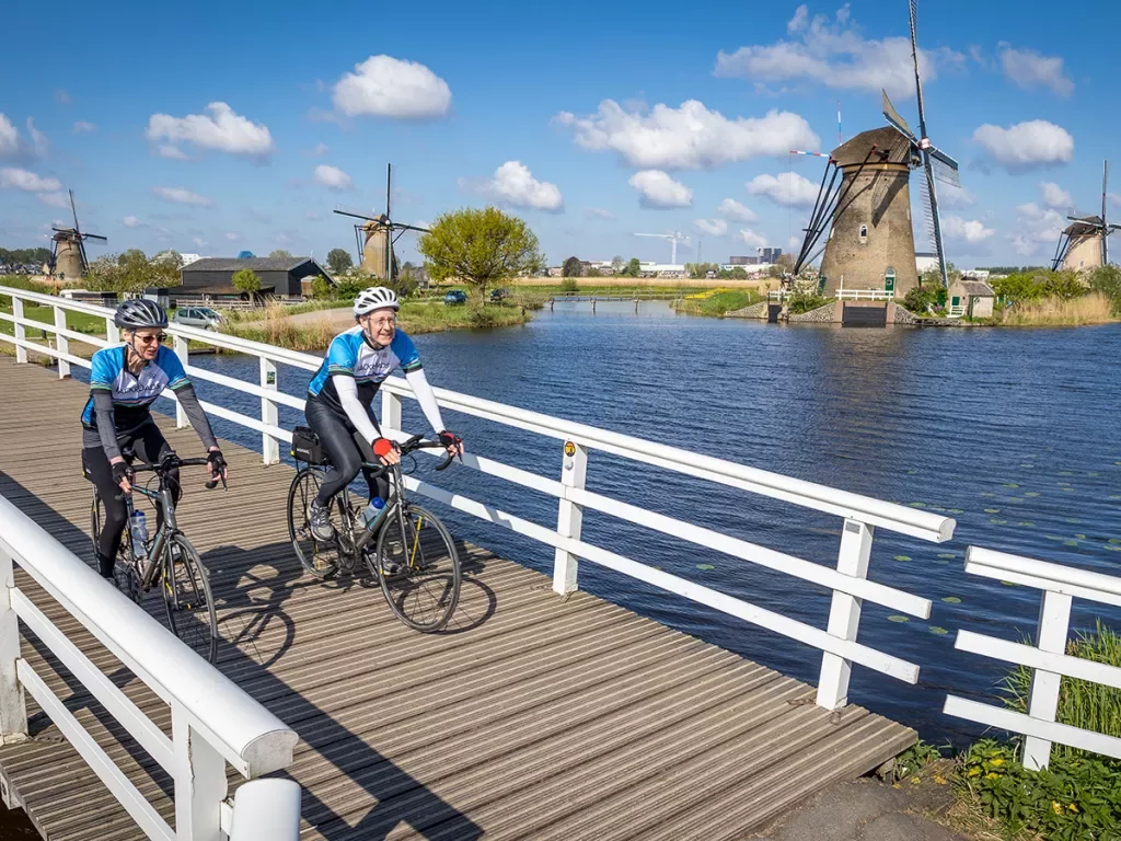 Bikers on small bridge with windmills in background