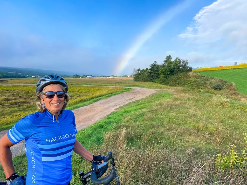 Guest smiling on trail in foreground, rainbow in background.